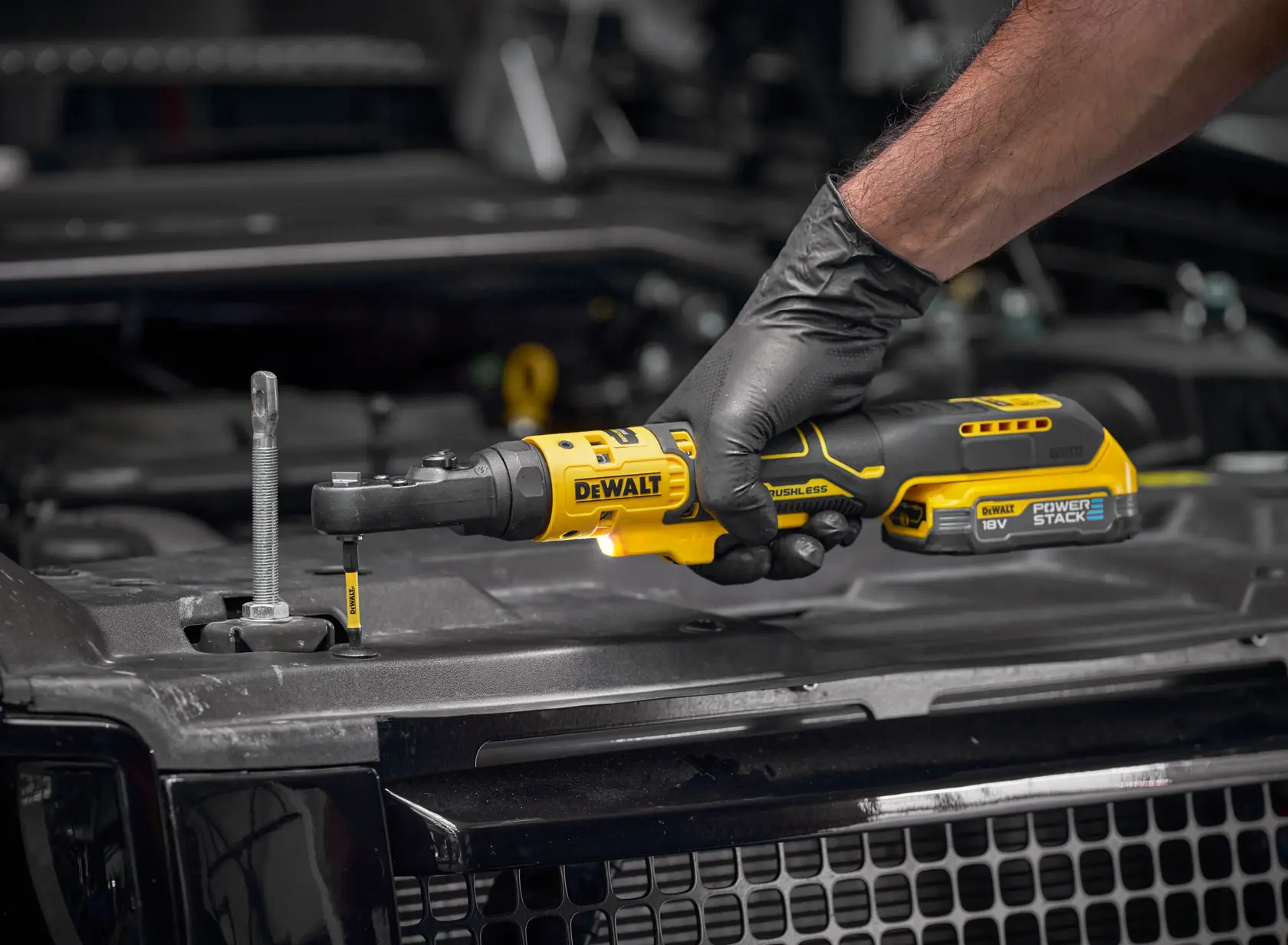 DEWALT ratchet tool in use; product SKUs DCF520N-XJ, DCF520N. Photography category. Gloved hand, car engine area.