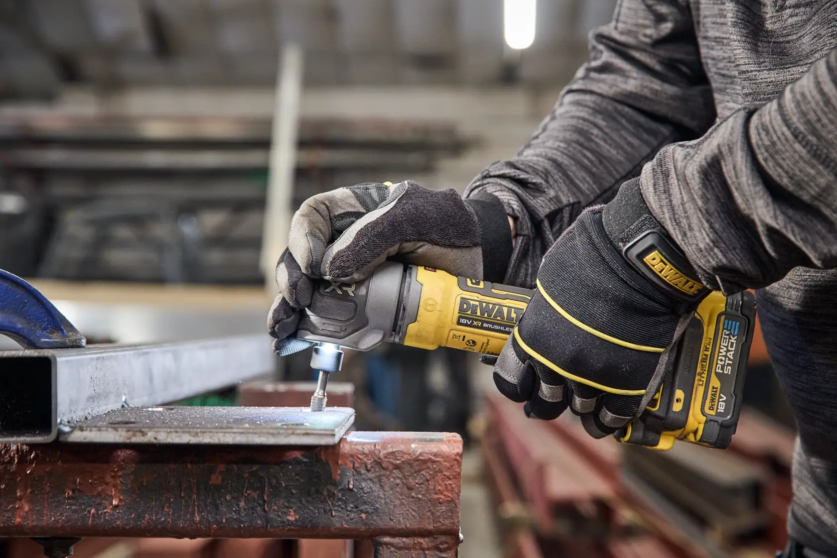 DEWALT tool in use on metal, showing DCG421N-XJ, DCG421N. Worker with gloves operating power tool.