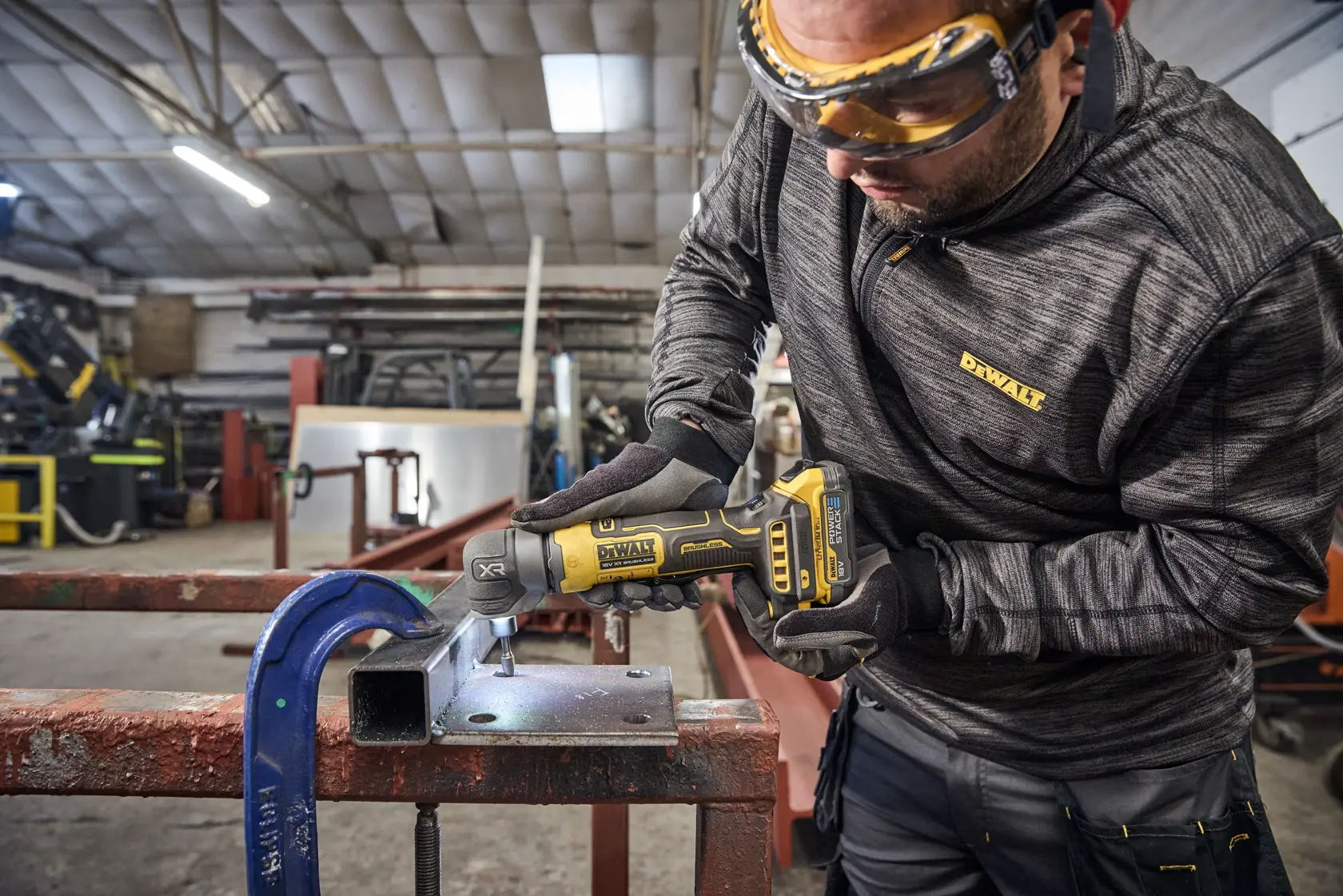 Worker uses DEWALT tool DCG421N-XJ, DCG421N on metal in workshop. Product for photography category.