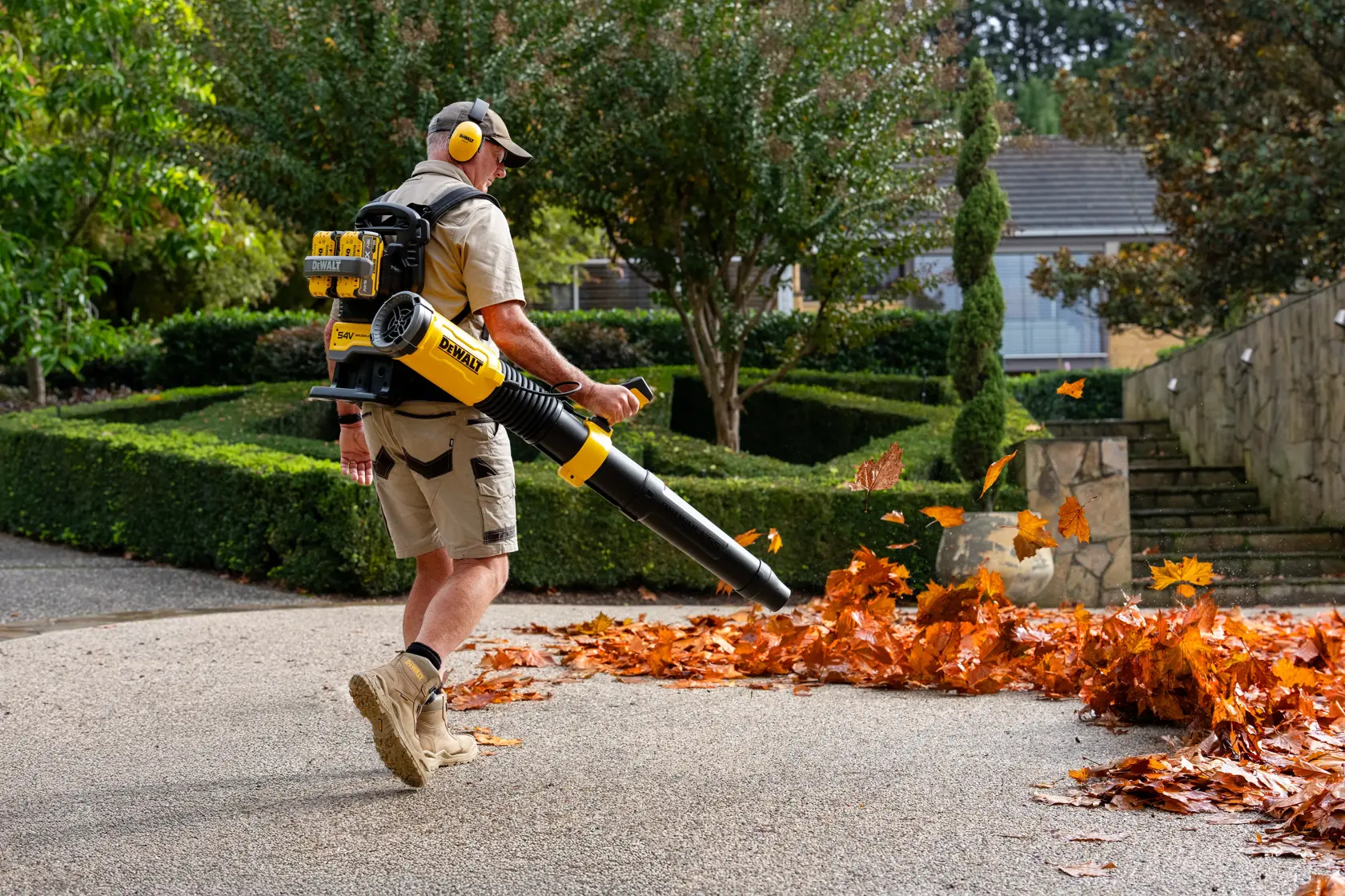 Person using a DEWALT backpack leaf blower to clear leaves from a paved garden path.