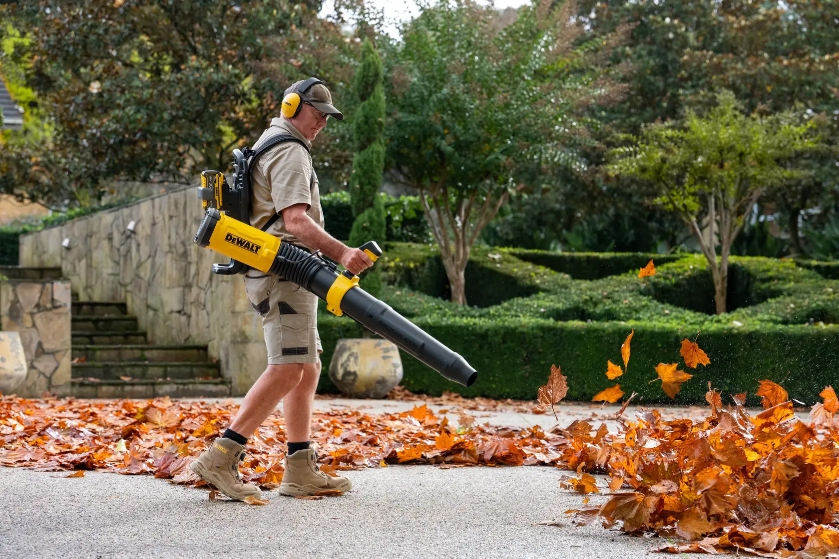 Person using a DEWALT cordless leaf blower to clear fallen leaves from a garden path.