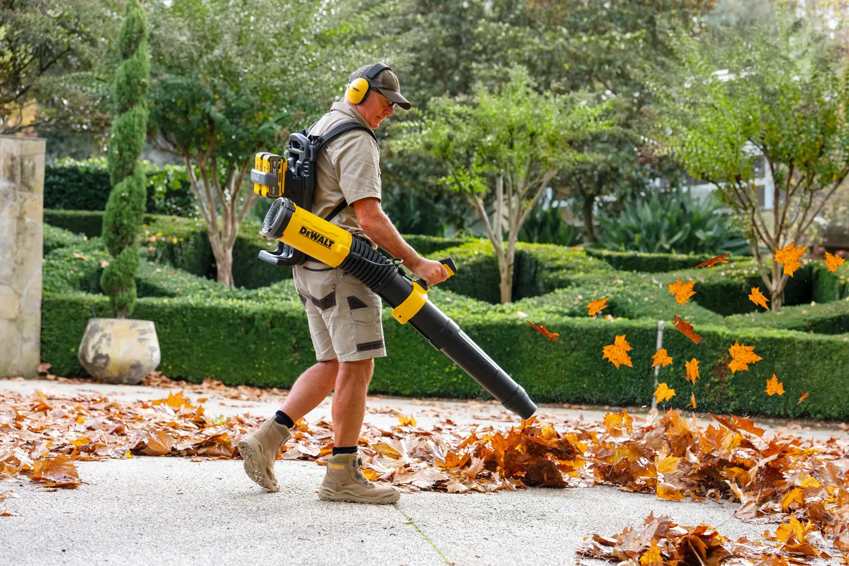 Person uses DEWALT battery-powered leaf blower to clear leaves outdoors.