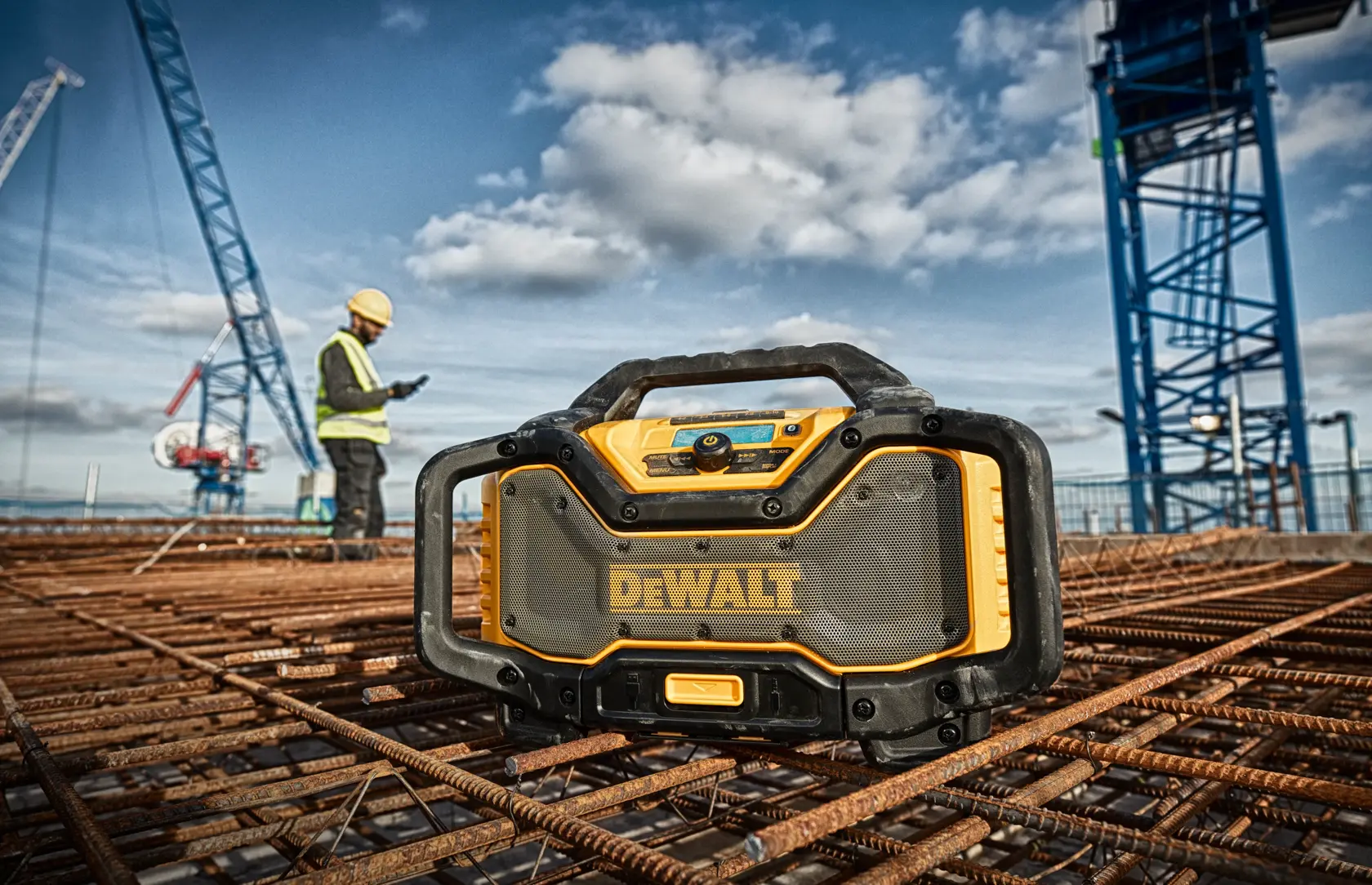 DEWALT jobsite radio on rebar at a construction site with cranes and worker in safety gear in the background.