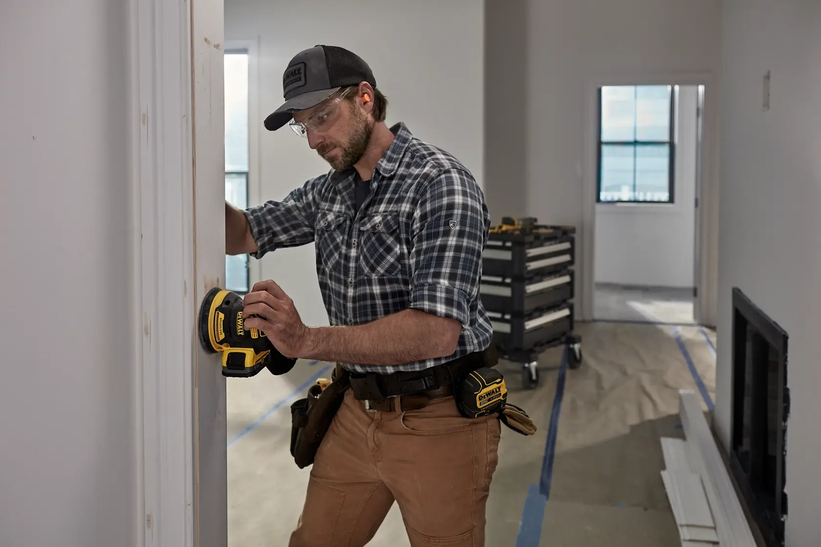 Person using DEWALT DCW210, DCW210D1 sander on door frame; tool belt visible; indoor workspace.