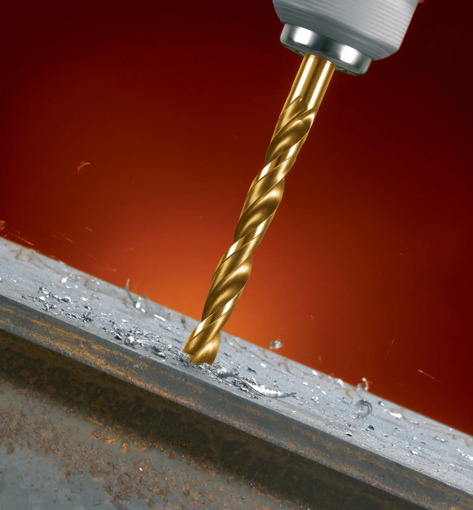 A close-up of a golden drill bit attached to a power drill, drilling into a metal surface with metal shavings and sparks visible.