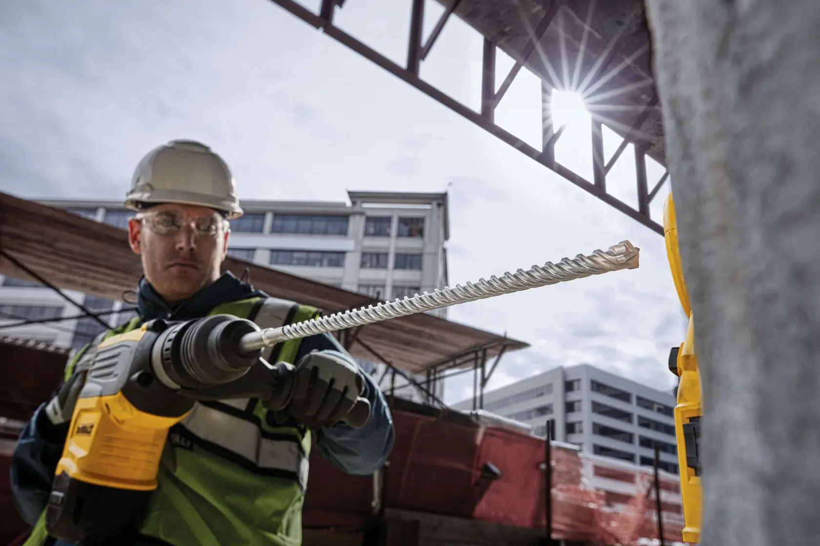 Worker using a DEWALT drill with DT60812 bit at a construction site. Buildings and sunlight in the background.