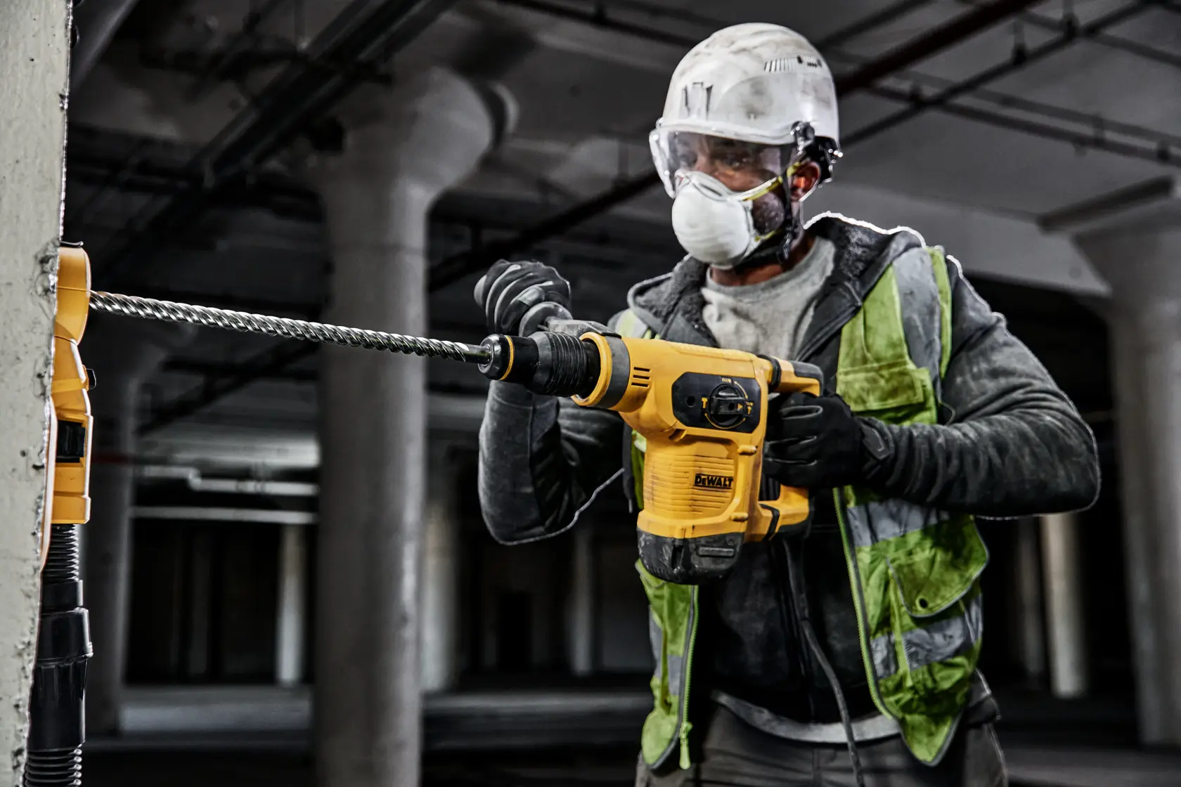 Worker using DEWALT rotary hammer drill in industrial setting, drilling into a concrete wall.