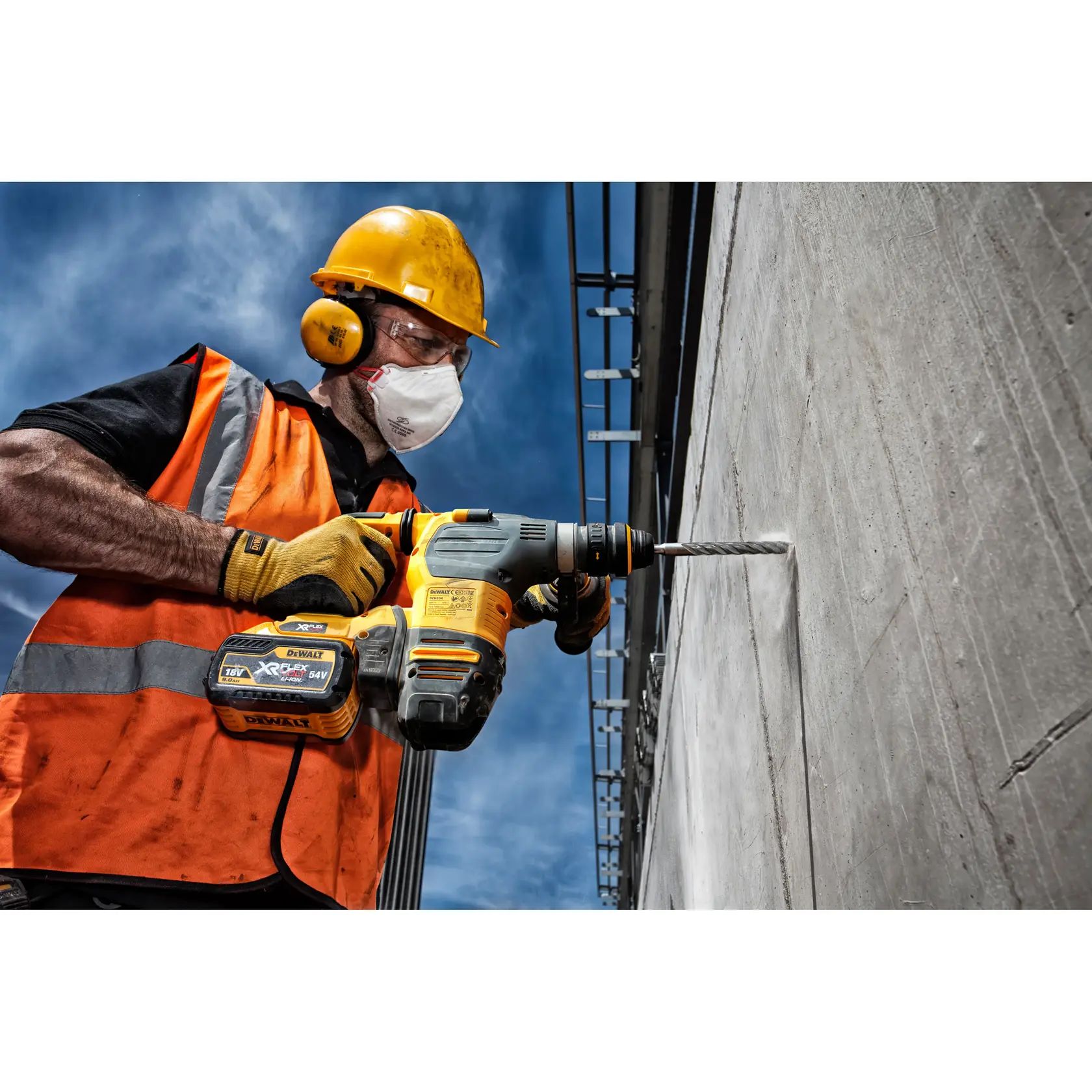 Worker uses DEWALT cordless drill to bore a hole in a concrete wall, wearing safety gear and an orange vest.
