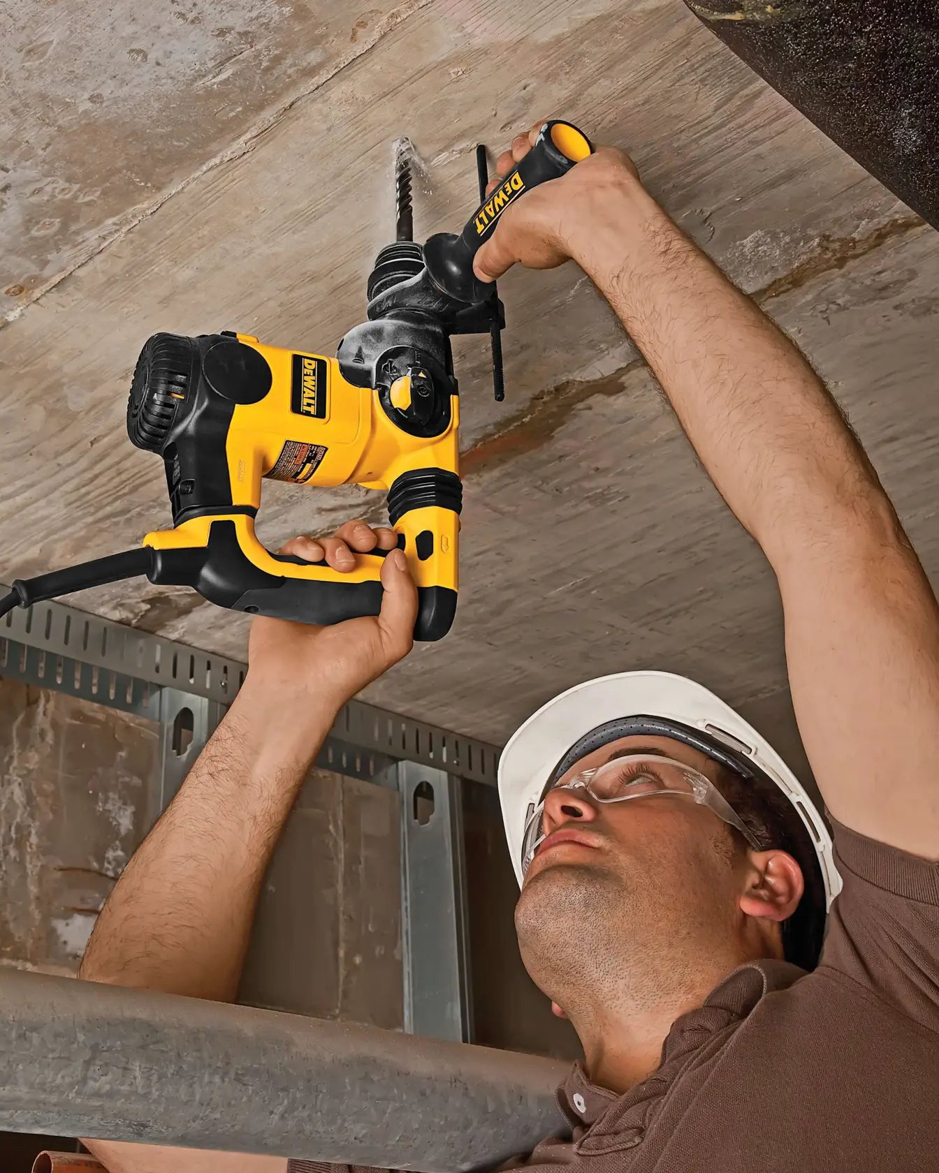 Person uses a DEWALT hammer drill on a ceiling, wearing a hard hat. The power tool is yellow and black.