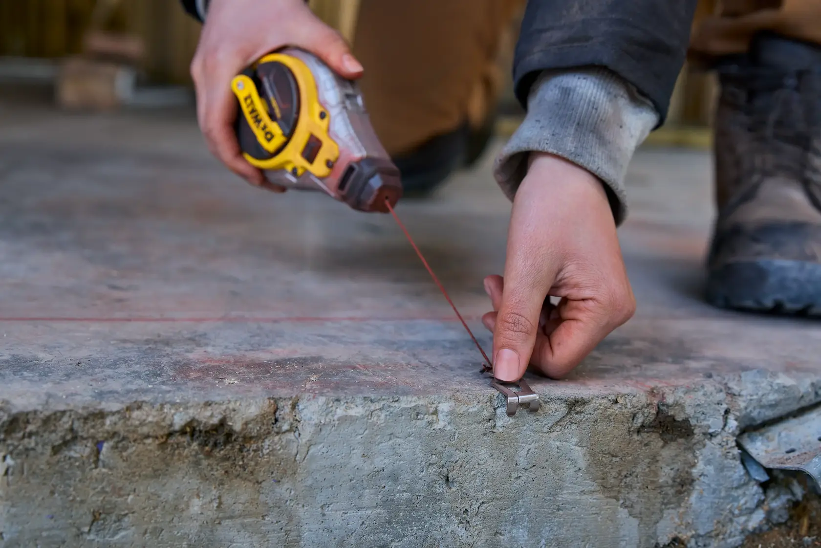 Close-up of a person using a DEWALT chalk line tool to mark a straight line on a concrete surface.